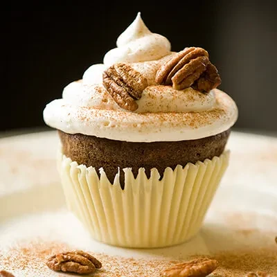 Dark cupcake with white frosting, cinnamon, and pecan halves.