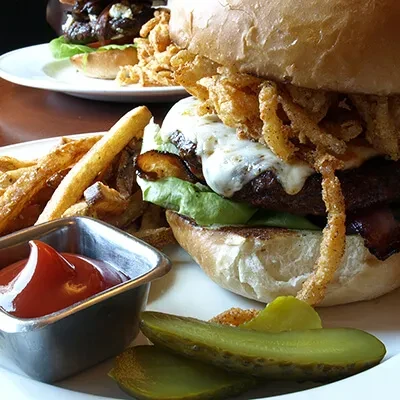 Hearty burger with onion rings, fries, ketchup, and pickles.
