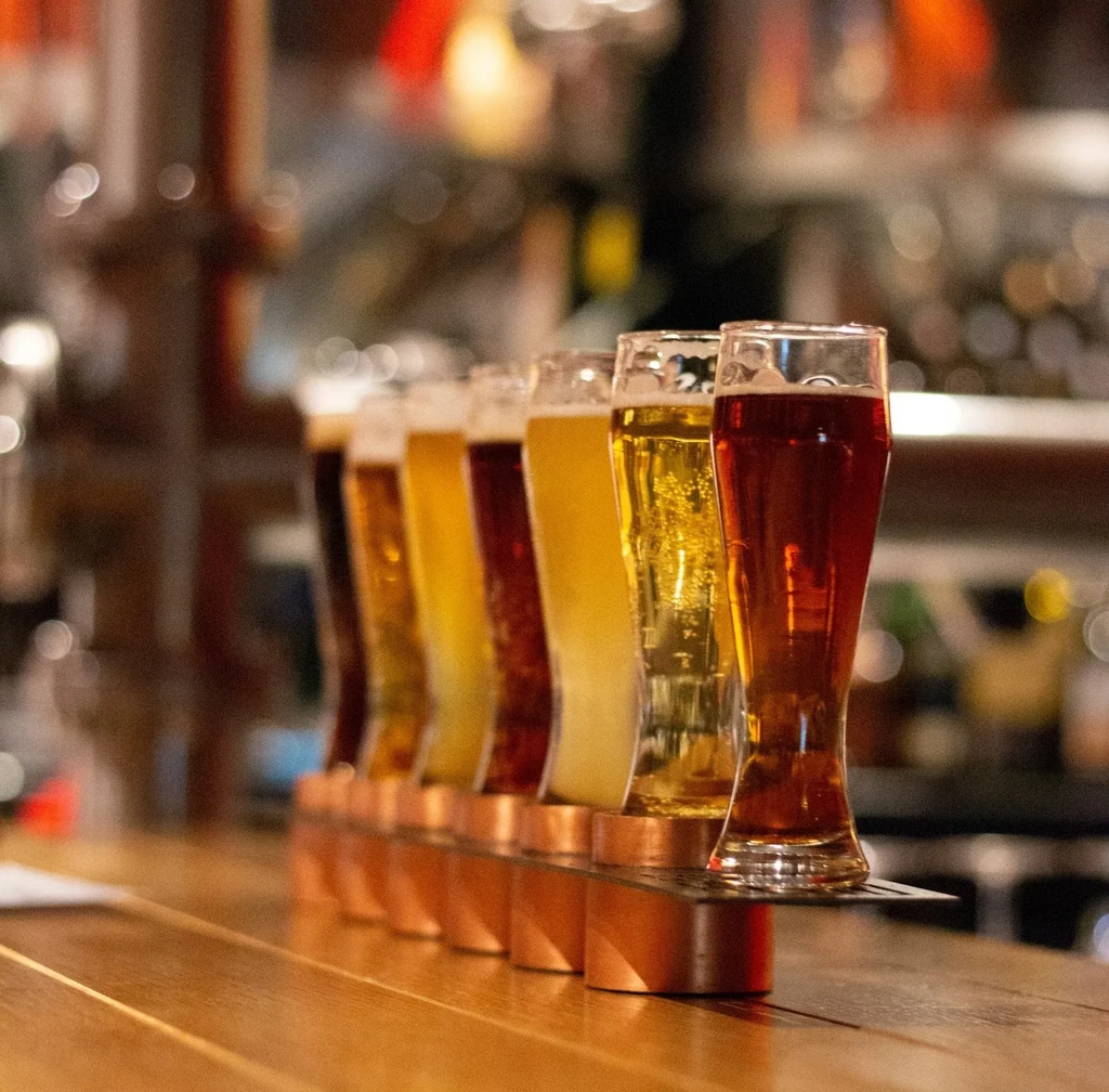 Six varied beers in a copper flight stand on a bar.