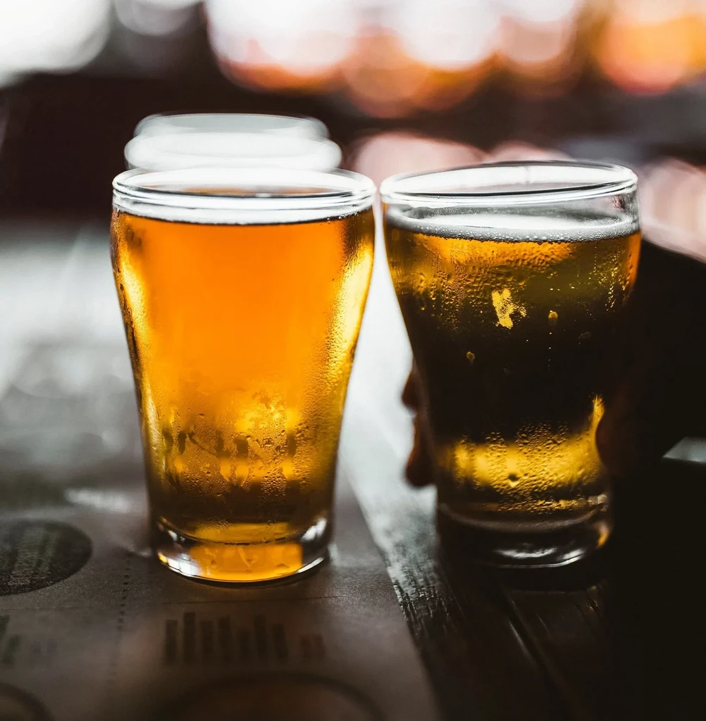 Two cold beers on a dark bar, one subtly held.
