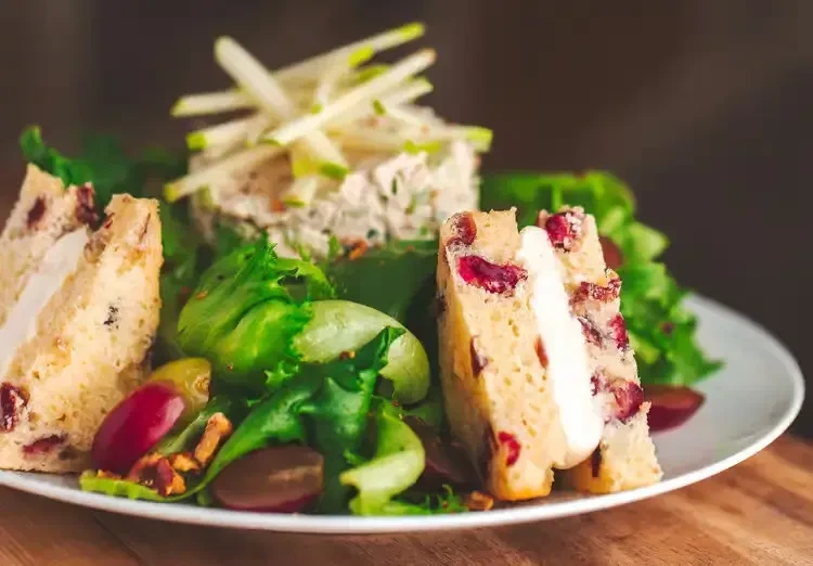 Gourmet green salad with chicken/tuna, apple, grapes, nuts, and savory bread.