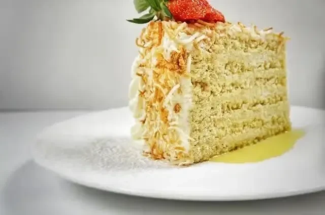 Slice of pistachio cake with whipped cream, coconut, strawberry, and sauce.