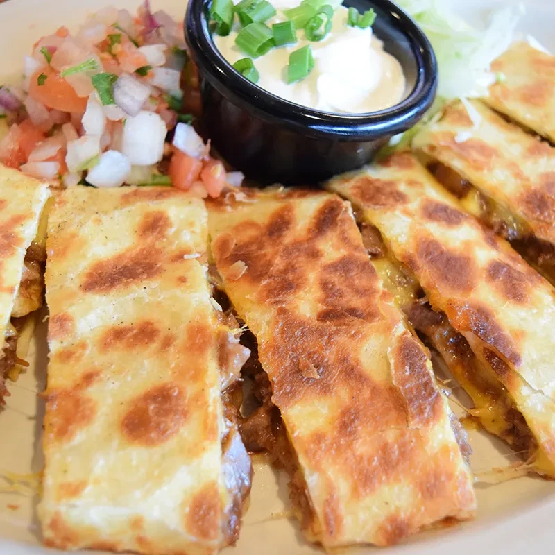 Sliced beef quesadillas with sour cream, pico de gallo, and lettuce.