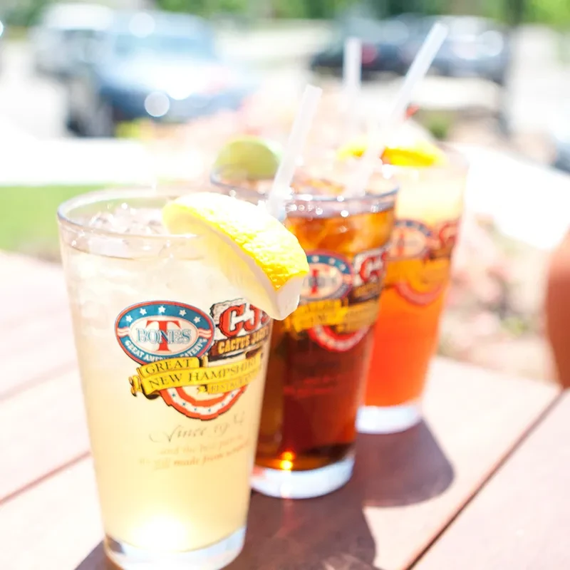 Three cold drinks with fruit, T-Bones and Cactus Jack's logos, outdoor table.