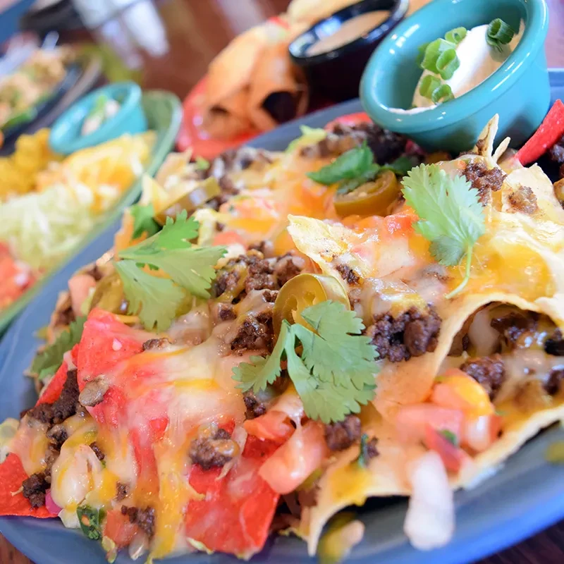 Loaded nachos with melted cheese, meat, jalapeños, and cilantro.