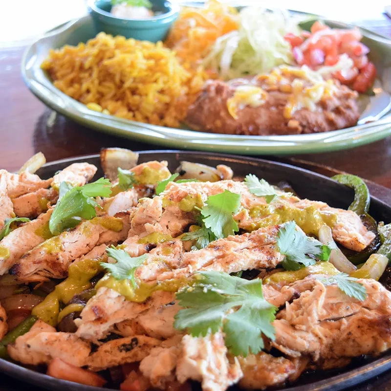 Sizzling chicken fajitas with onions, peppers, green sauce, and cilantro.
