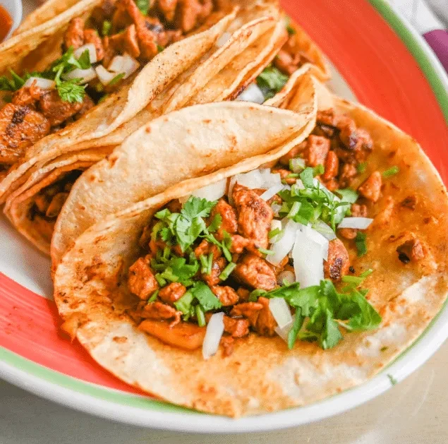 Three corn tacos with seasoned meat, cilantro, onions on a striped plate.