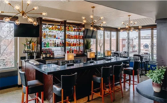 An empty, modern bar featuring a lit liquor display and winter windows.
