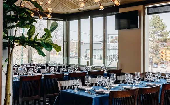Restaurant dining room with set tables, dark blue cloths, city view.