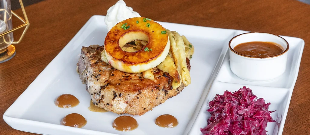 Plated pan-seared pork chop, grilled pineapple, red cabbage, and brown gravy.