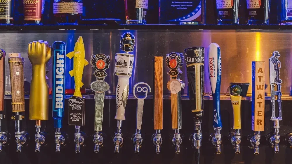 Colorful beer tap handles and illuminated spirit bottles at a bar.