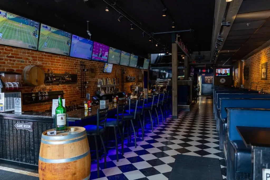 Empty sports bar interior with bar, TVs, blue booths, and checkerboard floor.