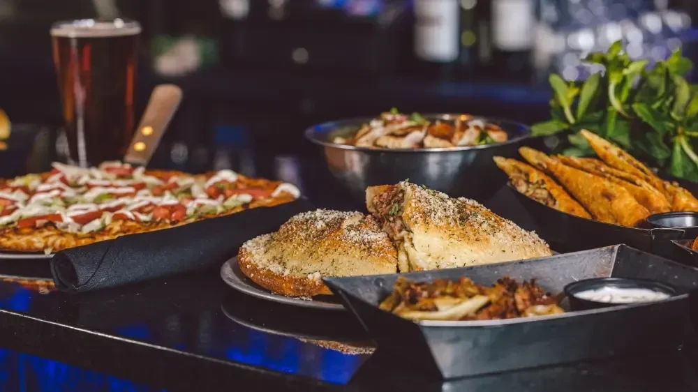 Pizza, savory pastries, fried dishes, and beer on a dark counter.