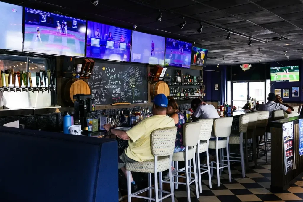 Lively sports bar interior: patrons, multiple TVs, checkerboard floor.