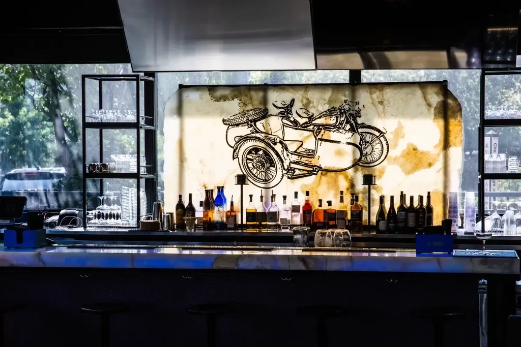Well-stocked bar with blue backlighting, vintage motorcycle art, and glassware.
