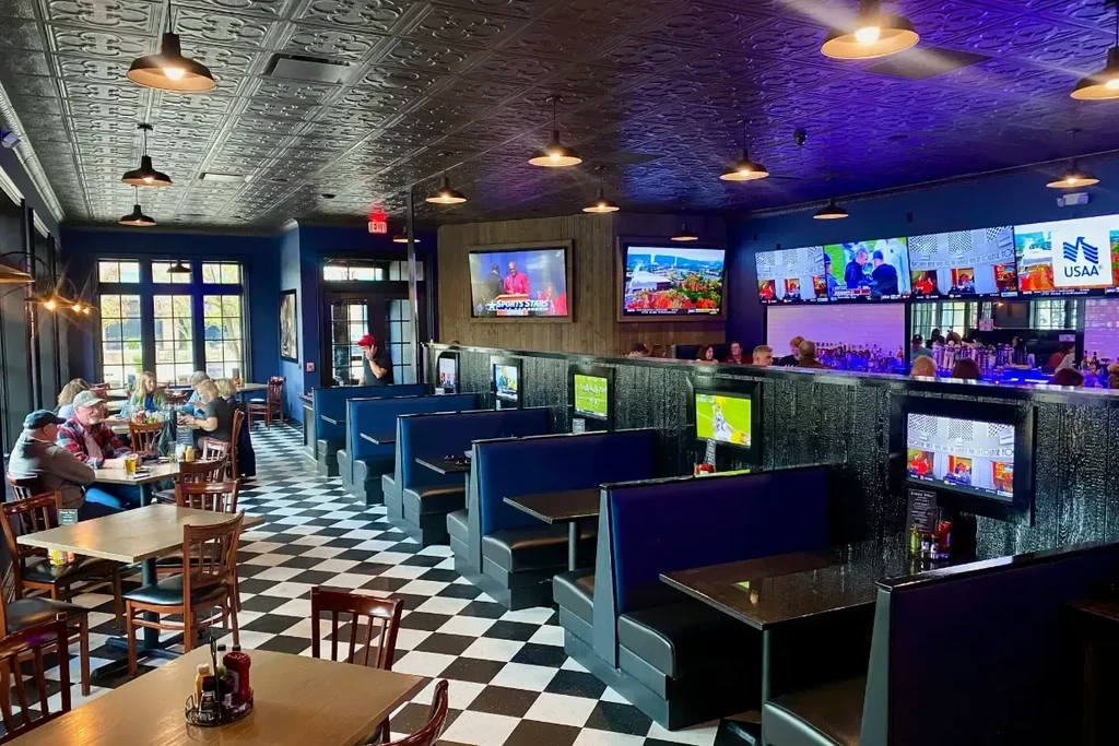 Lively sports bar interior with checkered floor, blue booths, and sports TVs.