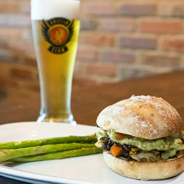 Rustic sandwich, asparagus, and beer on a wooden table.
