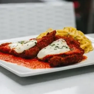 Chicken Parmesan with creamy pasta served on a white plate.