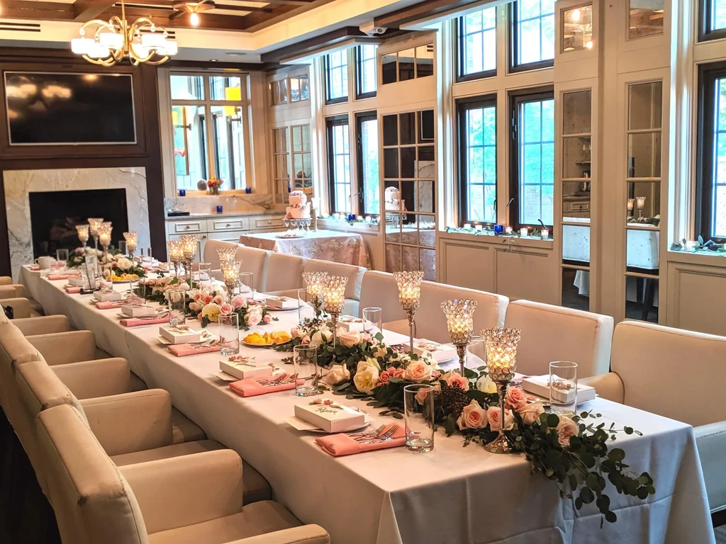 Long elegant dining table with pink floral garland, candles, and settings.