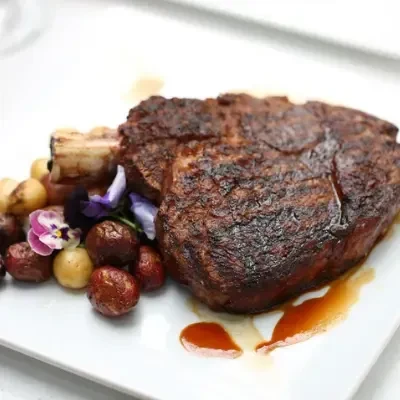 Seared steak, roasted potatoes, and edible flowers on a white plate.