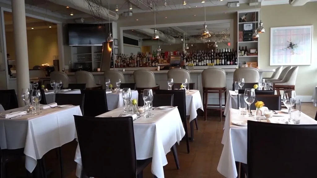 Elegant empty restaurant interior with set tables and a stocked bar.