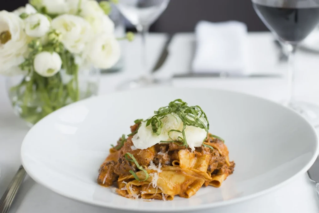 Pappardelle pasta with ragu, burrata, basil, and grated cheese.
