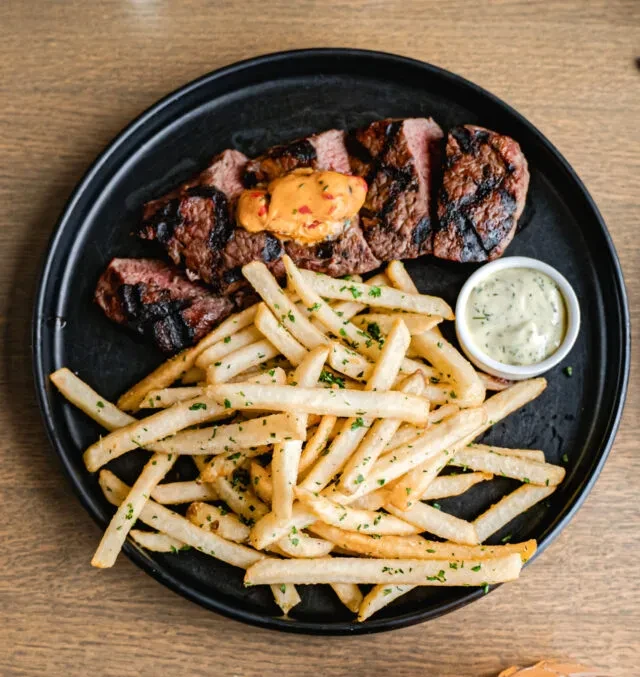 Sliced grilled steak, fries, chili sauce, and green herb dip.