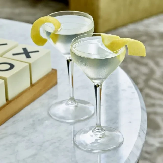 Two clear, frosty cocktails with lemon twists on a marble table.