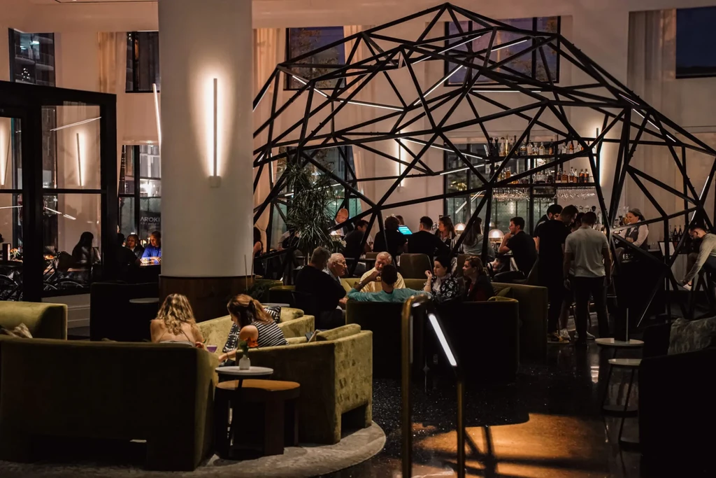Upscale bar, black geodesic frame encloses bar, olive seating, many patrons.
