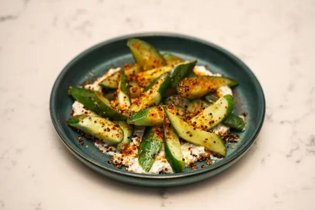 Sliced green vegetables, creamy sauce, and spice garnish on a teal plate.
