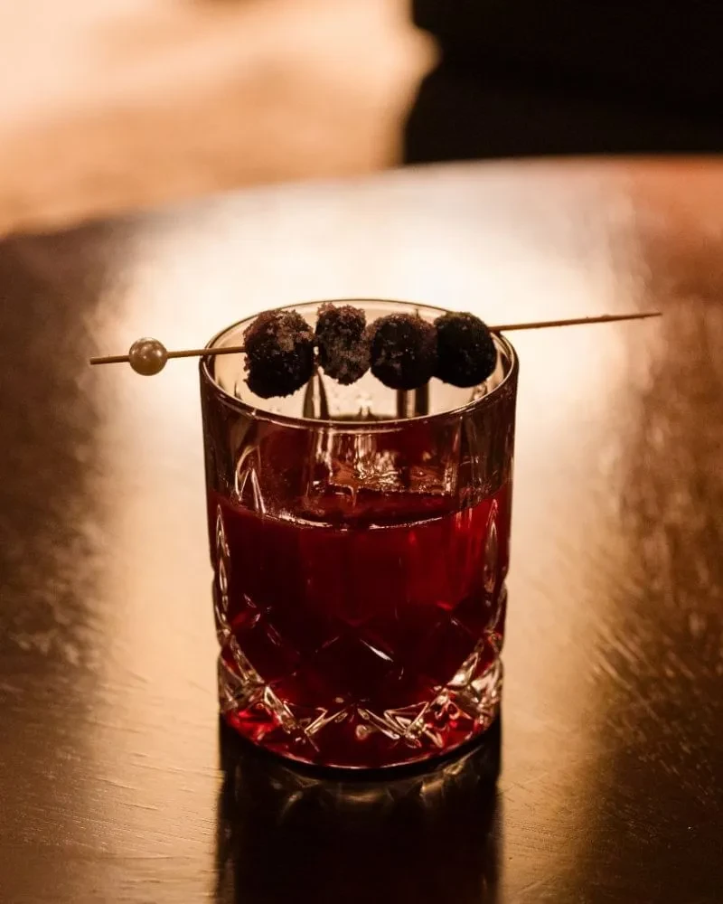 Dark red cocktail in a faceted glass with a sugared berry garnish.