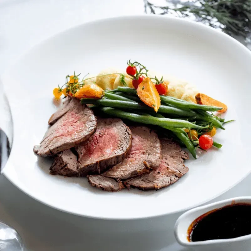Gourmet plate of medium-rare beef, green beans, mashed potatoes, and garnishes.