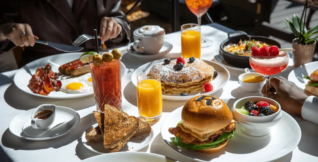 Two people enjoy an extensive brunch of eggs, pancakes, and cocktails.
