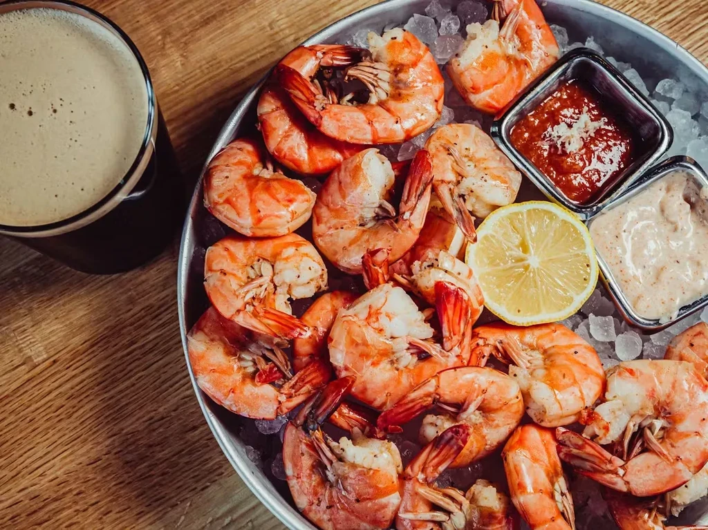 Shrimp cocktail platter with sauces, lemon, and dark beer on wood.