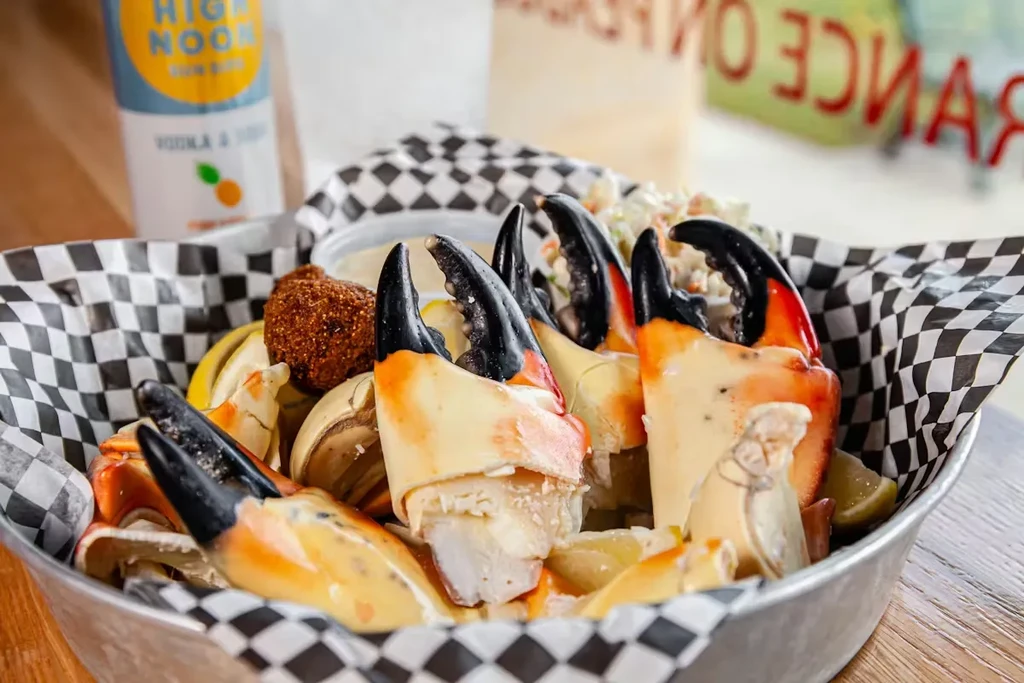 Pale stone crab claws with black tips, lemon, coleslaw, and hushpuppy.