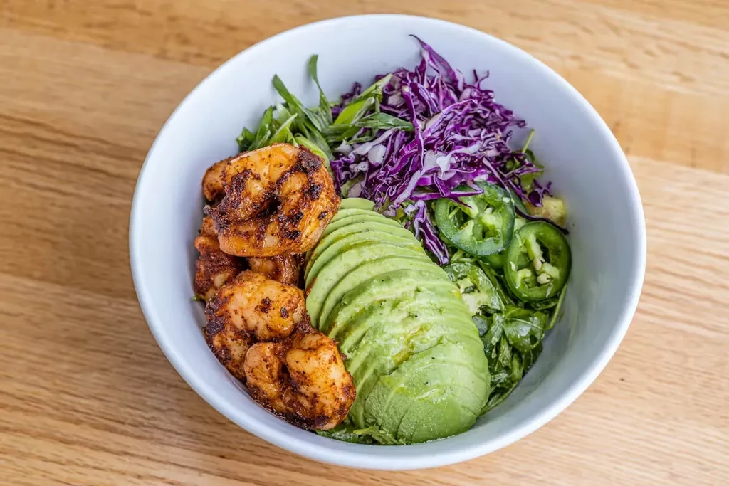 Food bowl with grilled shrimp, avocado, cabbage, jalapeños, and mixed greens.