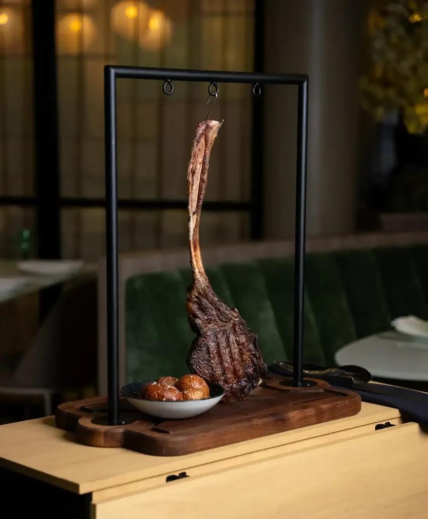 Hanging tomahawk steak with charred crust and roasted potatoes.