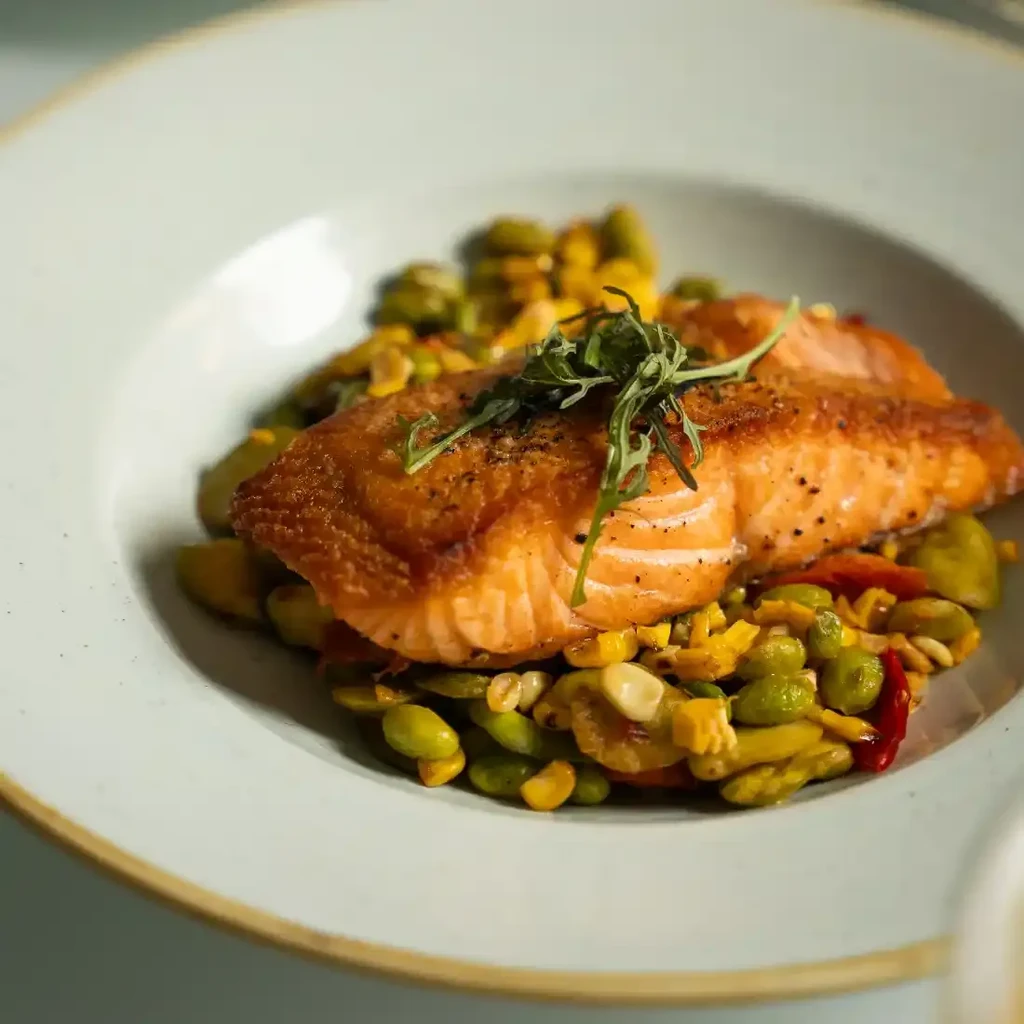 Plated grilled salmon with crispy skin, fresh herbs, and colorful vegetables.