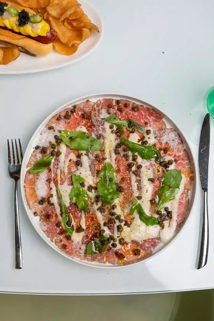 Beef carpaccio and gourmet hot dog with caviar and chips.