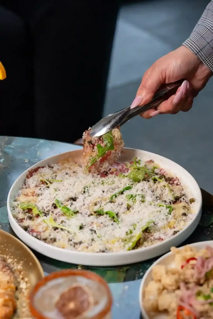 Tongs lift cheesy herb salad from a white plate.