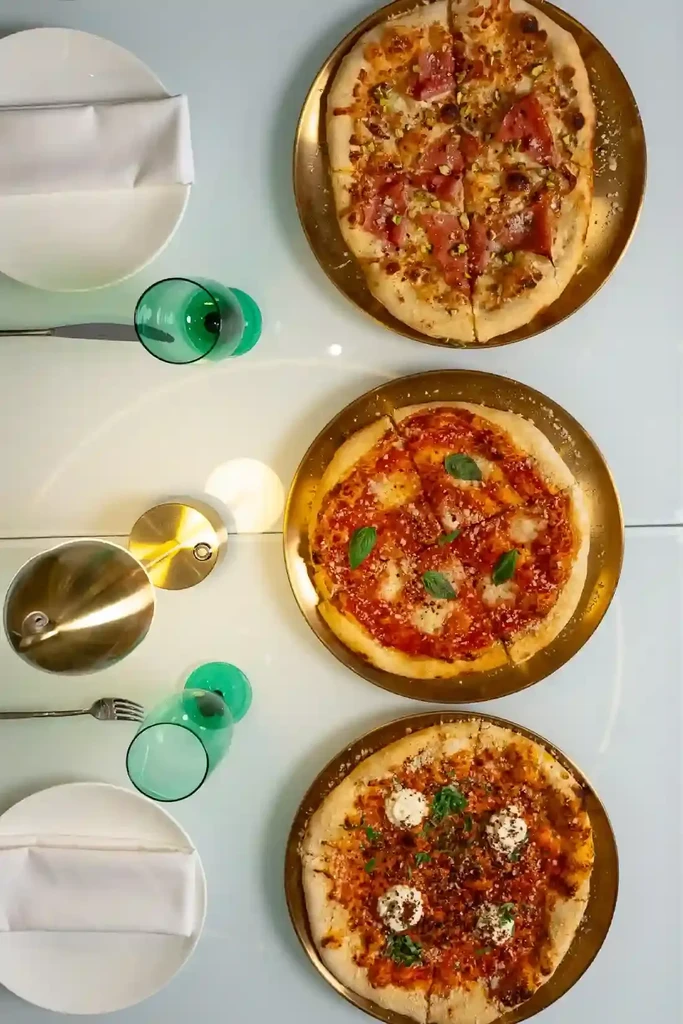 Three distinct pizzas and dining settings on a white table.