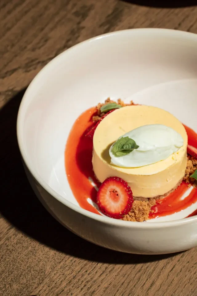 Plated pale yellow dessert with strawberry sauce, cream, and mint leaf.