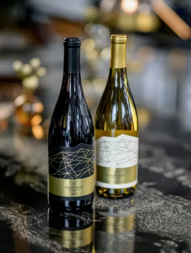Two wine bottles with matching gold mountain labels on a reflective surface.