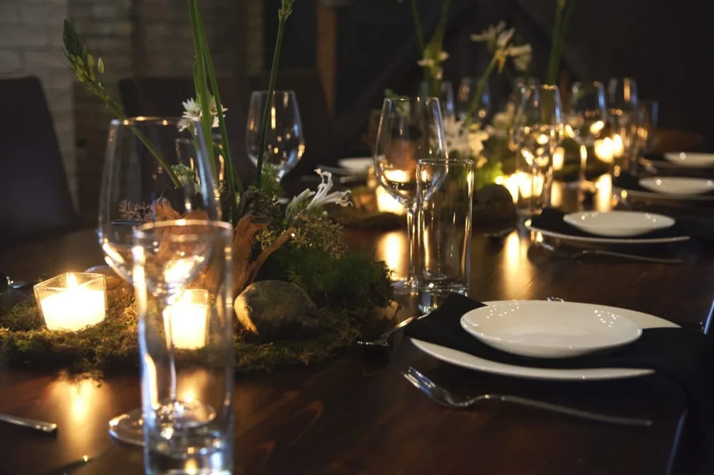 Candlelit table set with plates, glasses, and natural moss centerpieces.