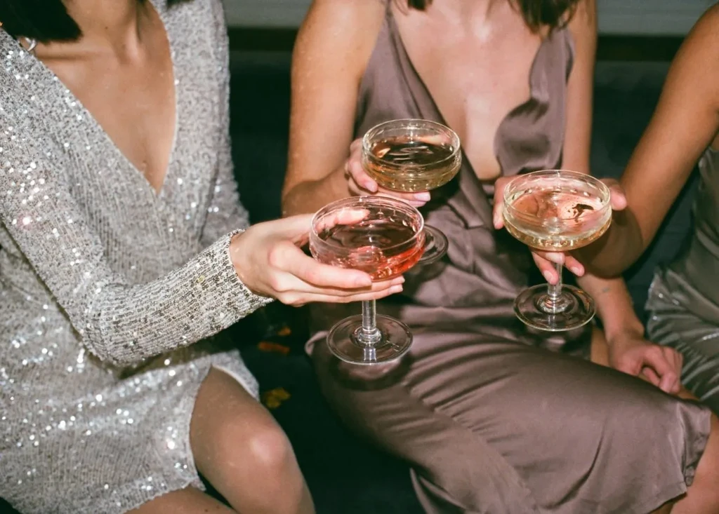 Close-up of three people holding drinks in elegant attire.