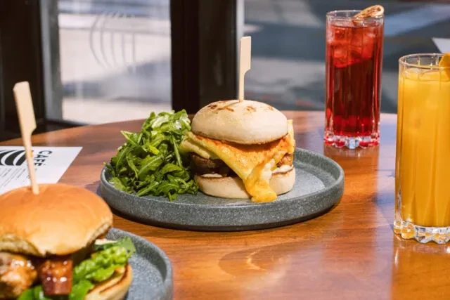 Burger with melted cheese, green salad, and two drinks.