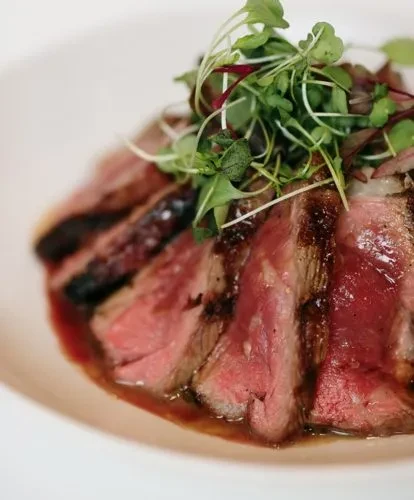 Plated medium-rare sliced meat with reddish-brown sauce and green garnish.
