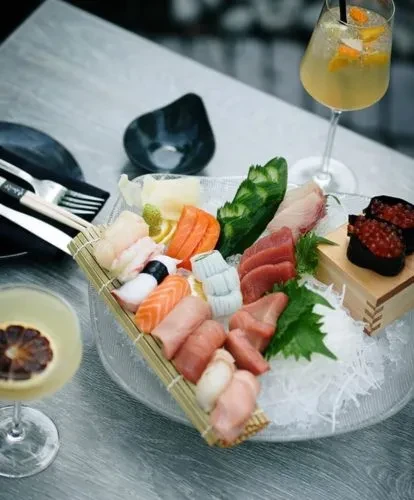 Platter of sushi and sashimi on ice with cocktails.