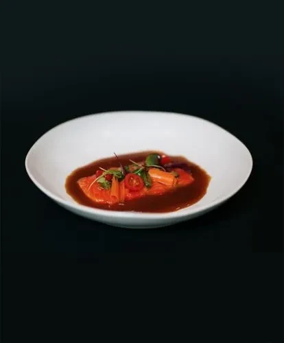 Beautifully plated salmon dish with sauce, carrots, tomatoes, and microgreens.