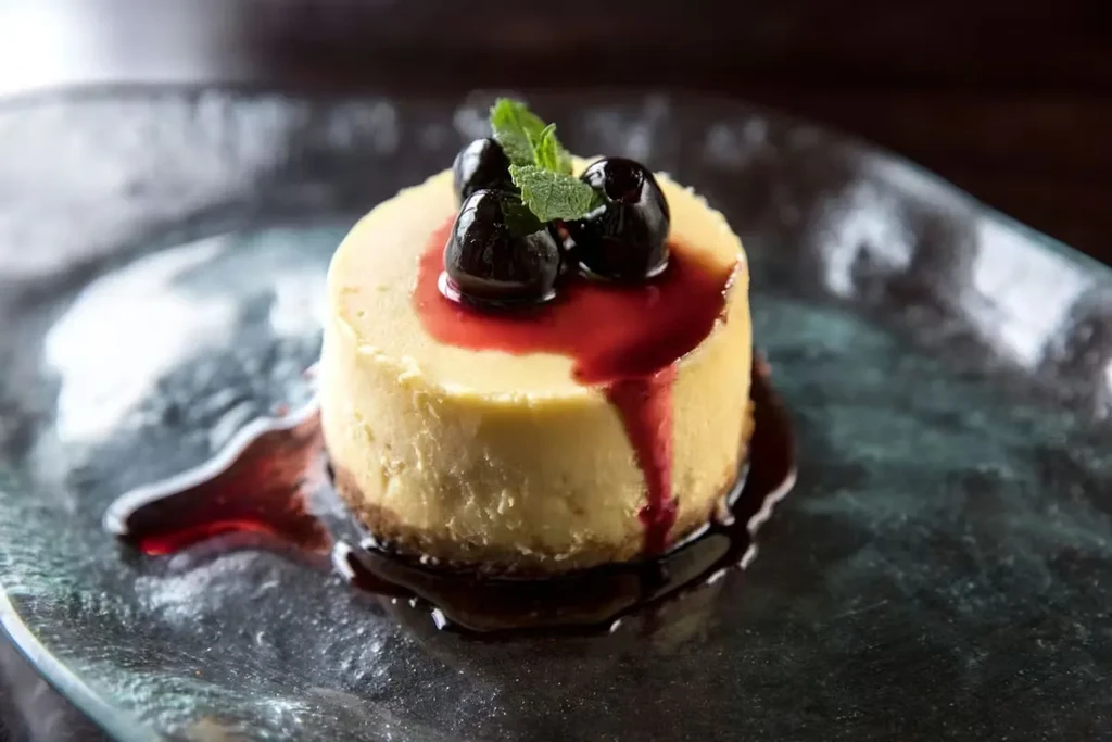 Creamy yellow dessert with dark berries, mint, and red sauce.